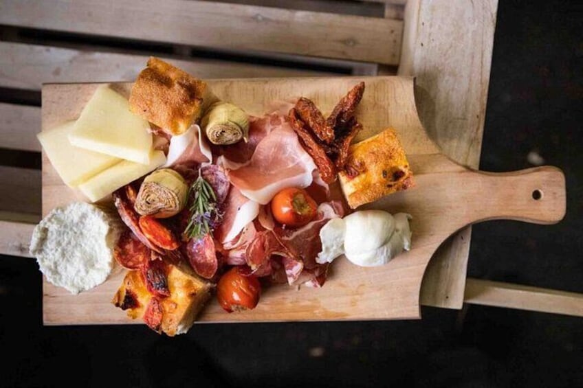 A wooden board with various cheeses, meats, and vegetables. 2