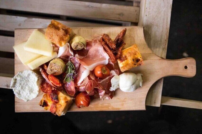 A wooden board with various cheeses, cured meats, and vegetables. 2