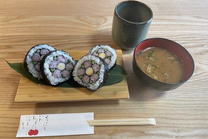 Sushi rolls on a wooden plate, a bowl of soup, and chopsticks on a table. 1