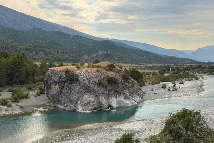 A river with a rocky outcrop in the middle, surrounded by mountains and greenery. 4