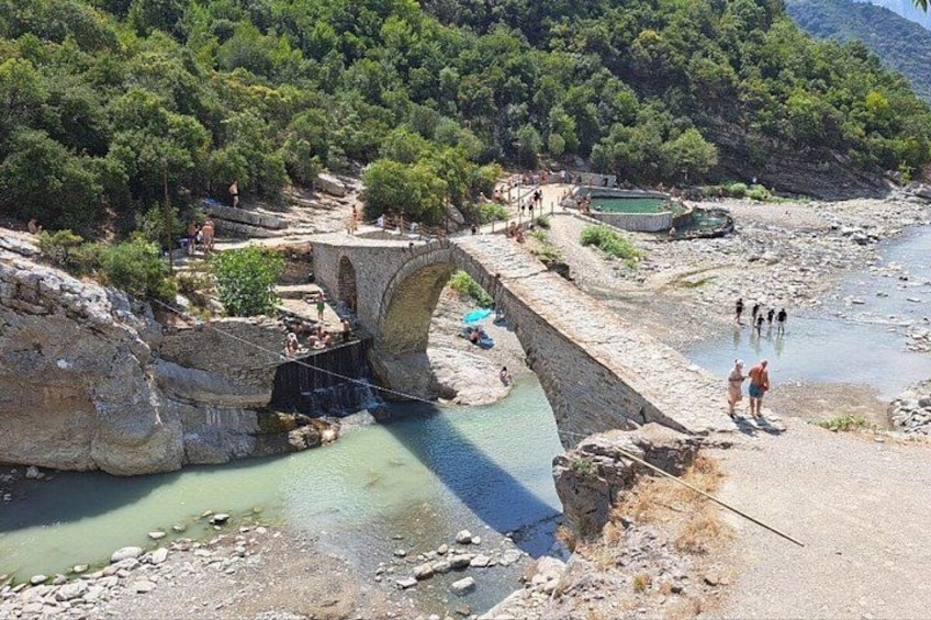 A stone bridge over a river, surrounded by greenery and rocky terrain. 3