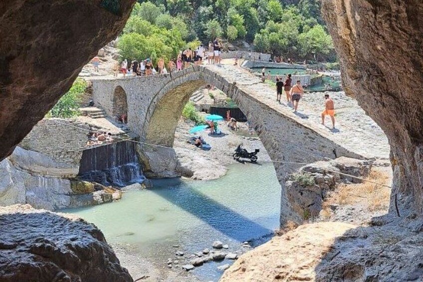 A stone bridge over a river with people walking and swimming below. 2
