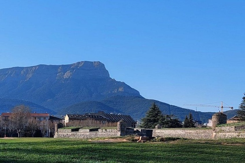A mountainous landscape with a clear sky, a grassy field, and several buildings. 4