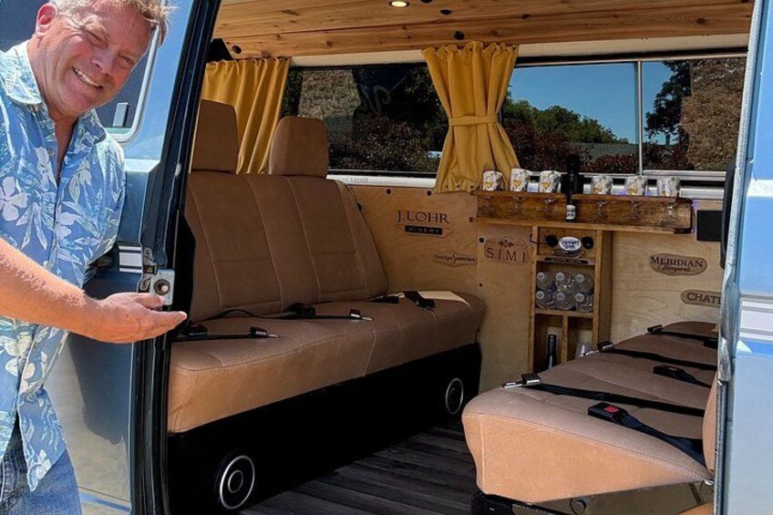 A camper van interior with a bed, seating area, and storage cabinets. 1