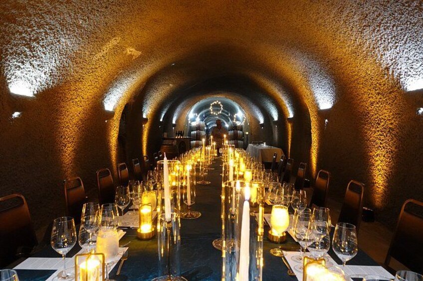 An underground dining room with tables set for a meal, candles, and wine glasses. 2