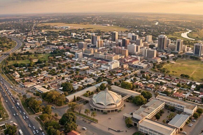 An aerial view of a city with a prominent circular building, a dense cluster of high-rise buildings, and a river in the background. 2