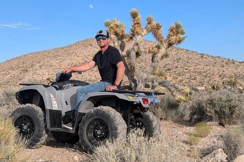 A person on an ATV in a desert landscape with cacti and a hill in the background. 2