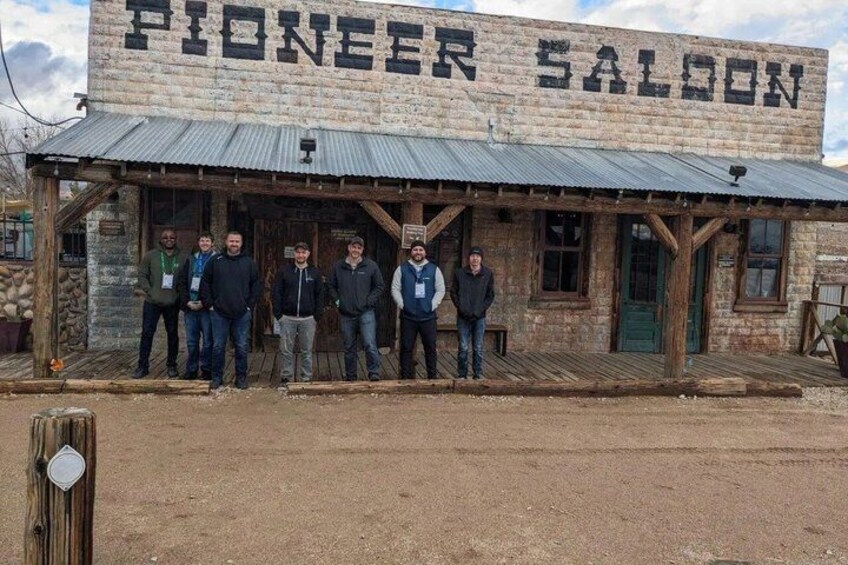 A rustic building with a sign reading 'PIONEER SALOON' and a group of people standing in front. 2