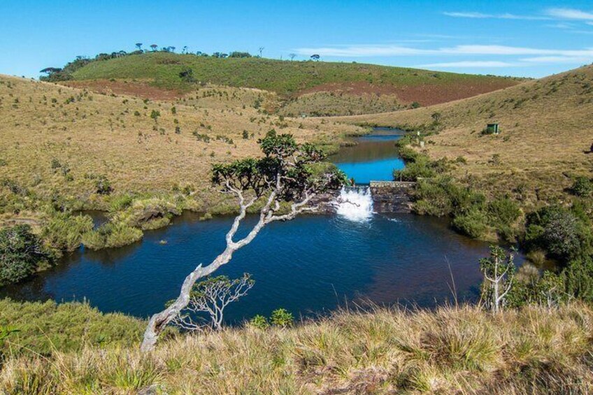 A river with a waterfall, surrounded by grassy hills and sparse trees. 1