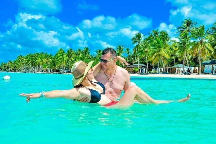 A couple in a tropical beach setting with clear turquoise water, palm trees, and a clear sky. 2