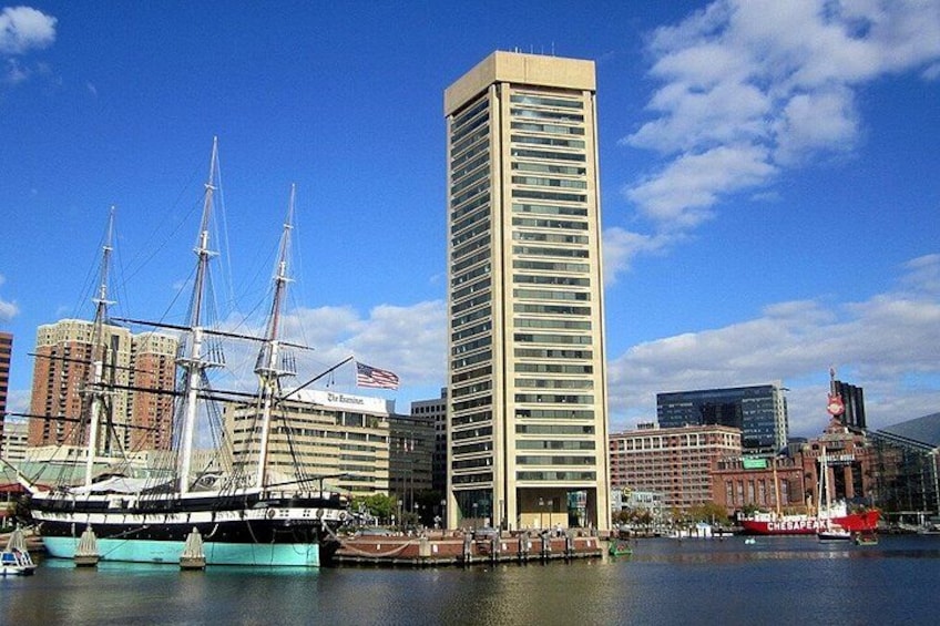 A tall building, a historic ship, and a modern skyscraper by a waterfront. 5