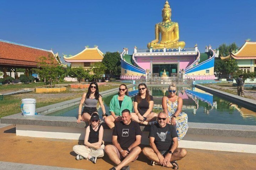 A group of people posing in front of a golden Buddha statue with traditional architecture in the background. 3