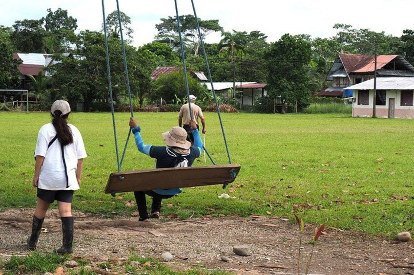 A swing set in a grassy field with a few people. 2