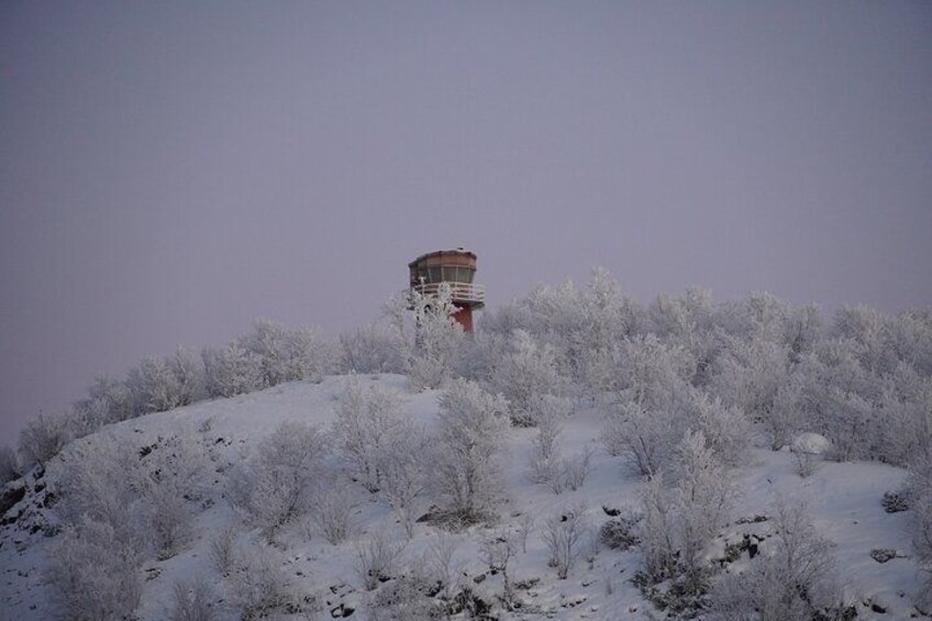 A snow-covered hill with sparse vegetation and a structure with a cylindrical top. 2