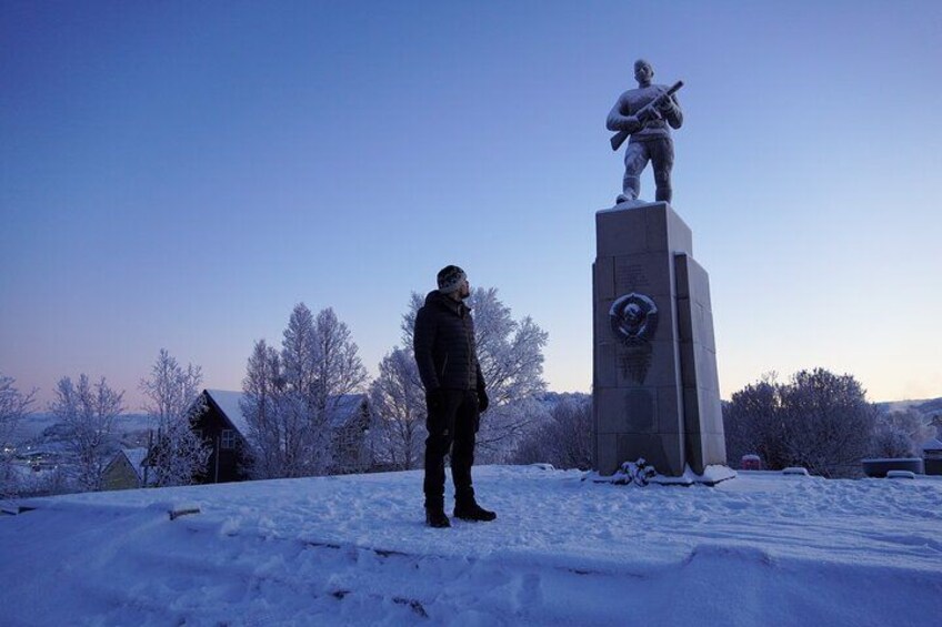 A person standing in a snowy landscape with a statue of a soldier on a pedestal. 4