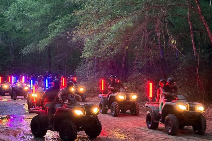 A group of off-road vehicles with illuminated lights driving through a forested area. 2