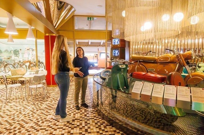 A museum interior with vintage motorcycles on display, a patterned floor, and a red pillar. 5