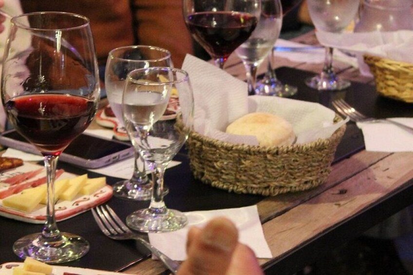 A dining table with wine glasses, plates, and a basket with bread. 5