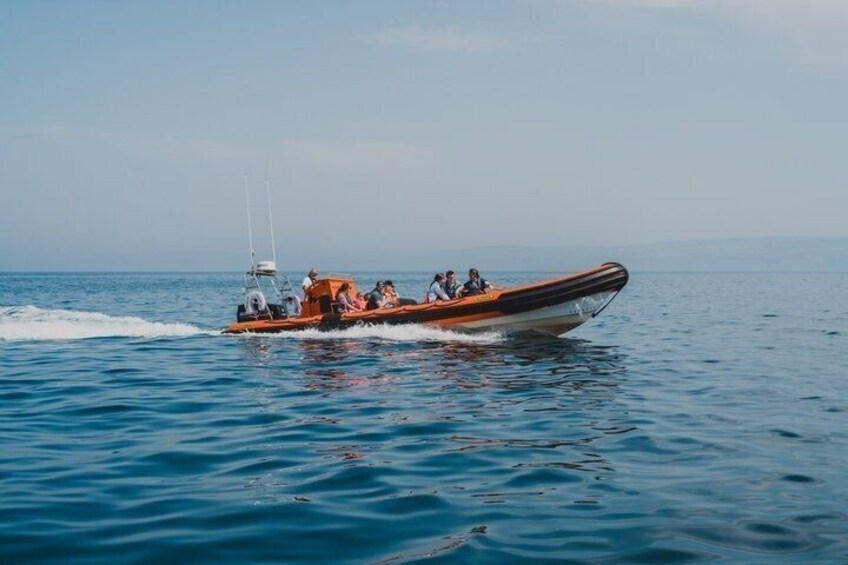A small orange boat with people on it, moving through calm blue water. 5