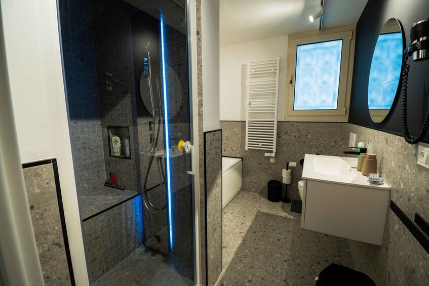 A modern bathroom with a glass shower enclosure, a white bathtub, a vanity with a mirror, and a window. 5