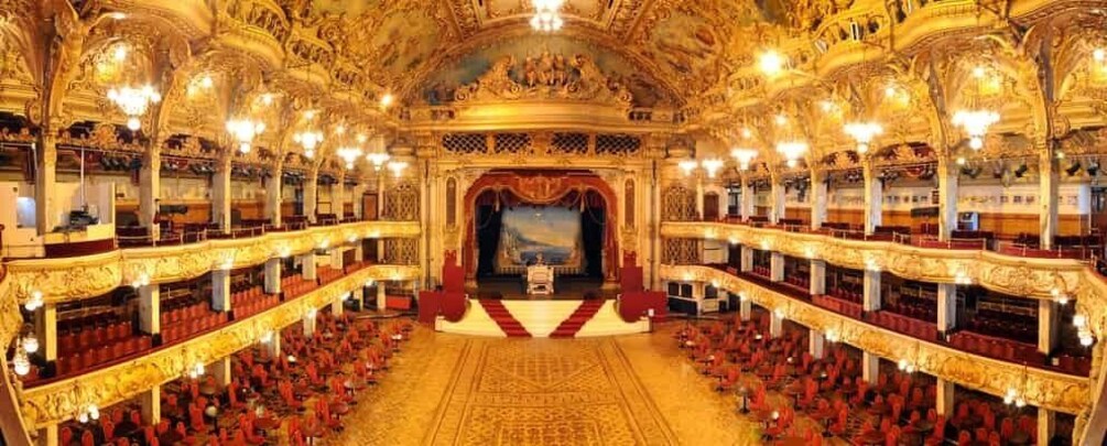 An ornate theater with a grand stage, multiple balconies, and intricate ceiling designs. 5