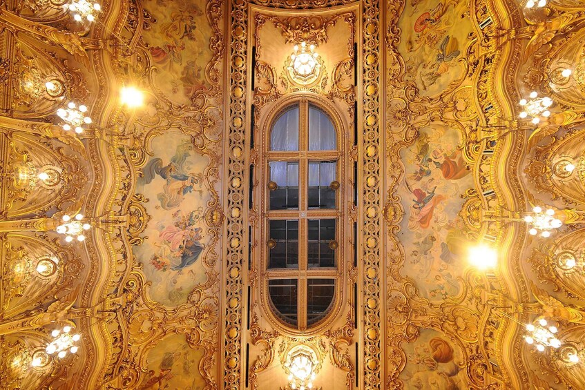 An ornate room with elaborate gold decorations, a large window, and multiple chandeliers. 4