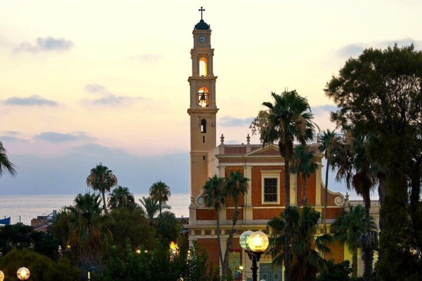 A church with a tall bell tower, palm trees, and a body of water in the background. 5
