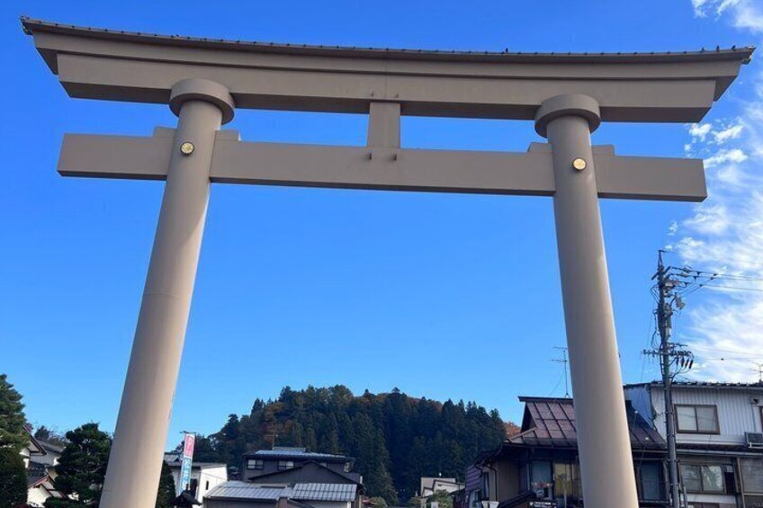 A torii gate with a clear blue sky and a forested hill in the background. 5