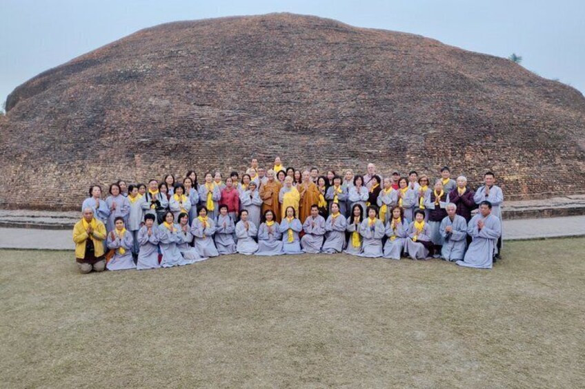 A group of people in traditional attire posing in front of a large, ancient stone structure. 3