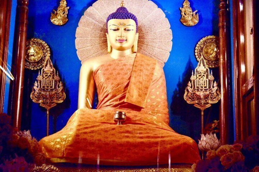 A seated Buddha statue with a blue backdrop, surrounded by ornate golden decorations. 5