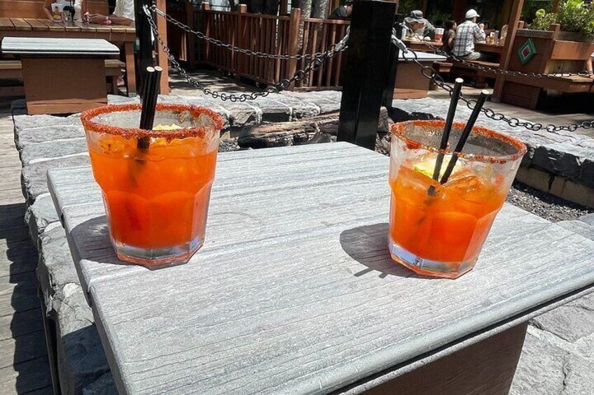 Two glasses of orange beverage on a wooden table with a chain barrier in the background. 1