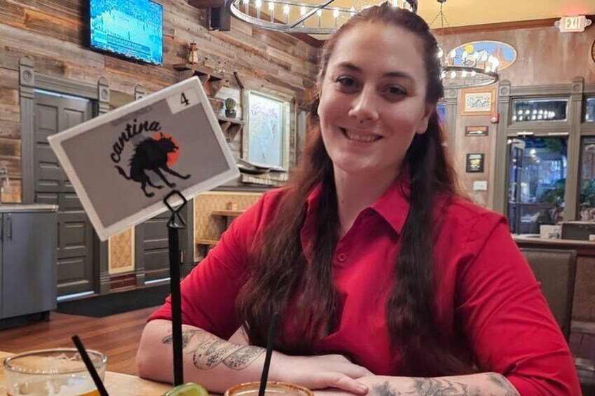 A person sitting at a table with a drink, a card with a bull logo, and a TV screen in the background. 3