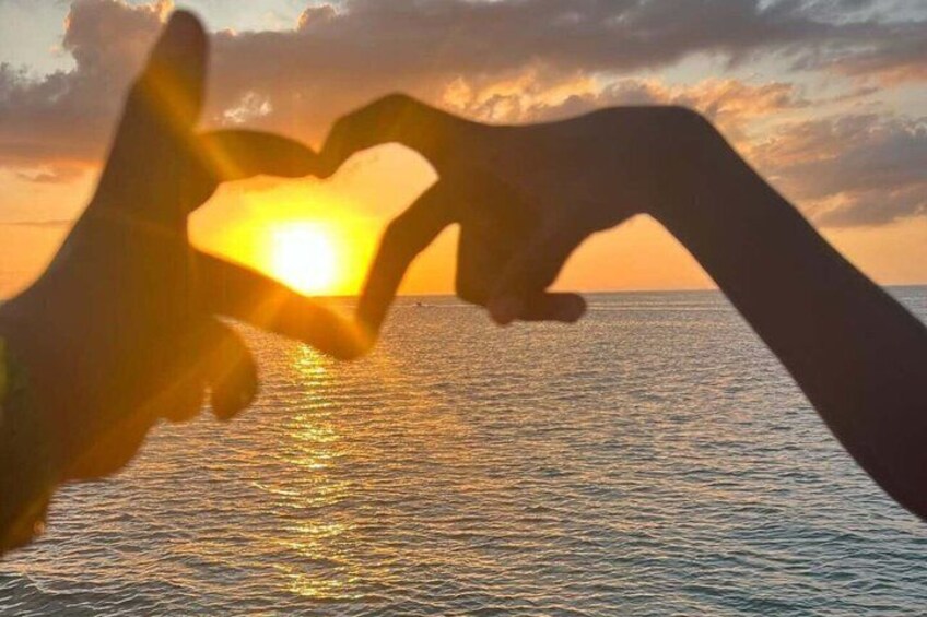Hands forming a heart shape with the sun setting in the background. 3
