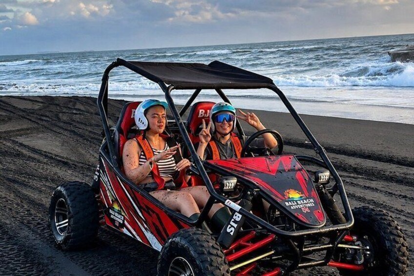Two people in a dune buggy on a beach with the ocean in the background. 4