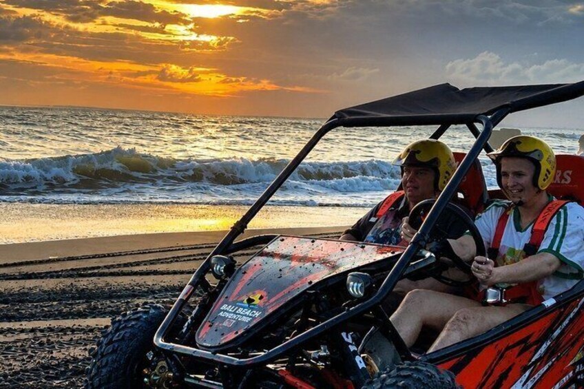 Two people in a dune buggy on a beach with waves and a sunset in the background. 1