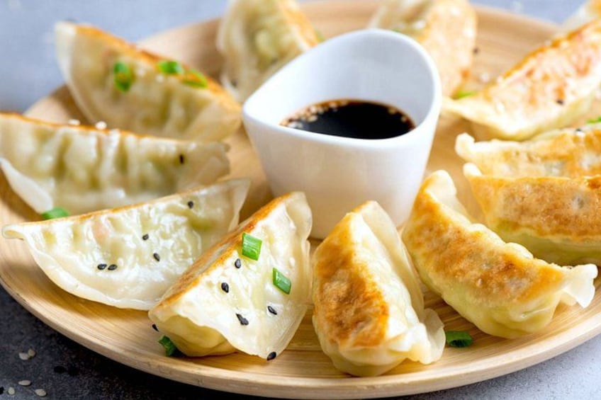 A plate of dumplings with a dipping sauce and green onions. 4