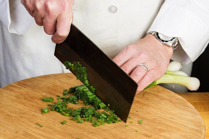 A person chopping green vegetables on a wooden cutting board. 2