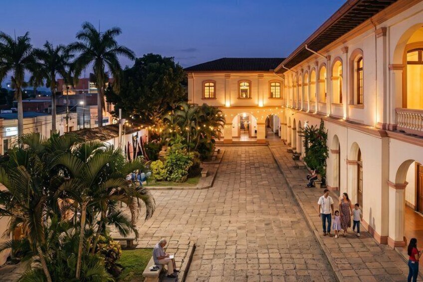 A courtyard with palm trees, a fountain, and people walking. 2