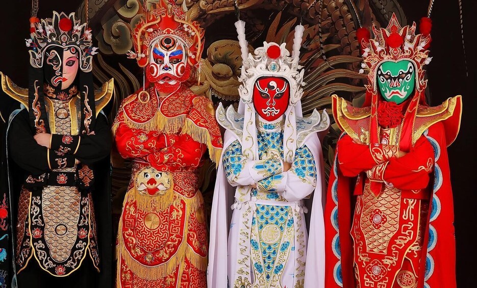 Four individuals in traditional Chinese opera costumes with elaborate headpieces and masks. 2