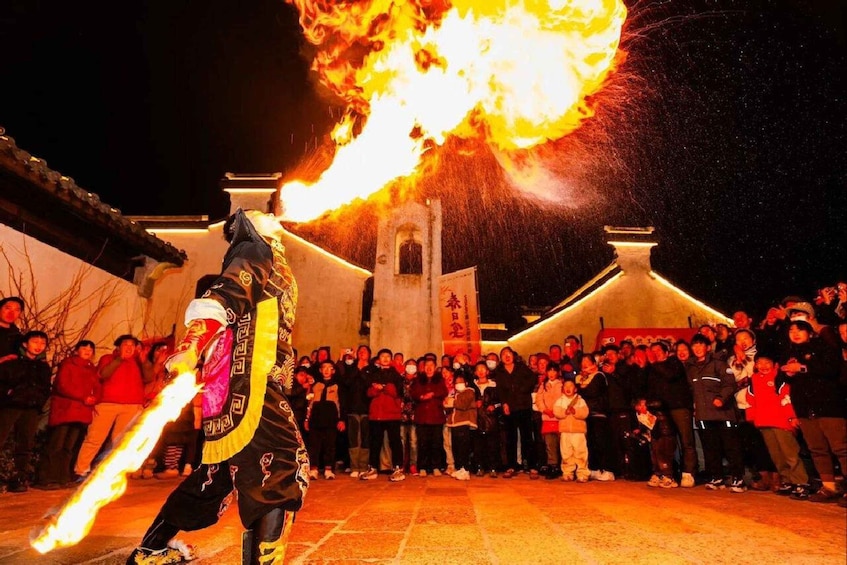 A performer with a flaming object in a traditional costume, a crowd watching, and a building with a bell tower in the background. 3