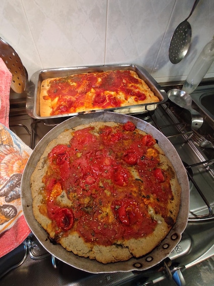 Two pizzas on a stove, one in a pan and one in a tray. 4
