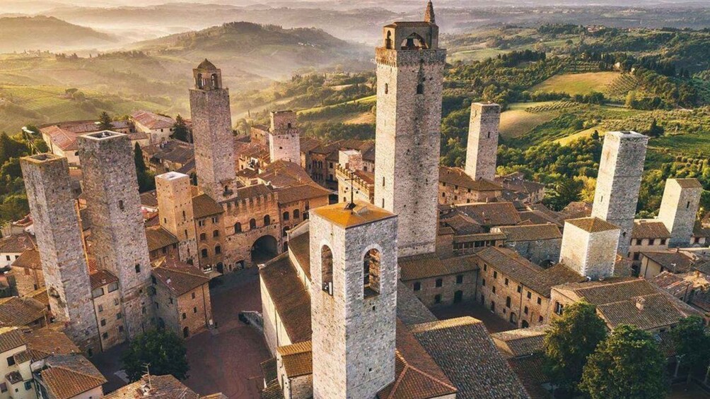 A medieval town with stone buildings and towers, surrounded by rolling hills and vineyards. 5