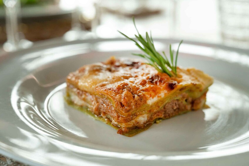 A slice of lasagna on a plate with a sprig of rosemary on top. 3