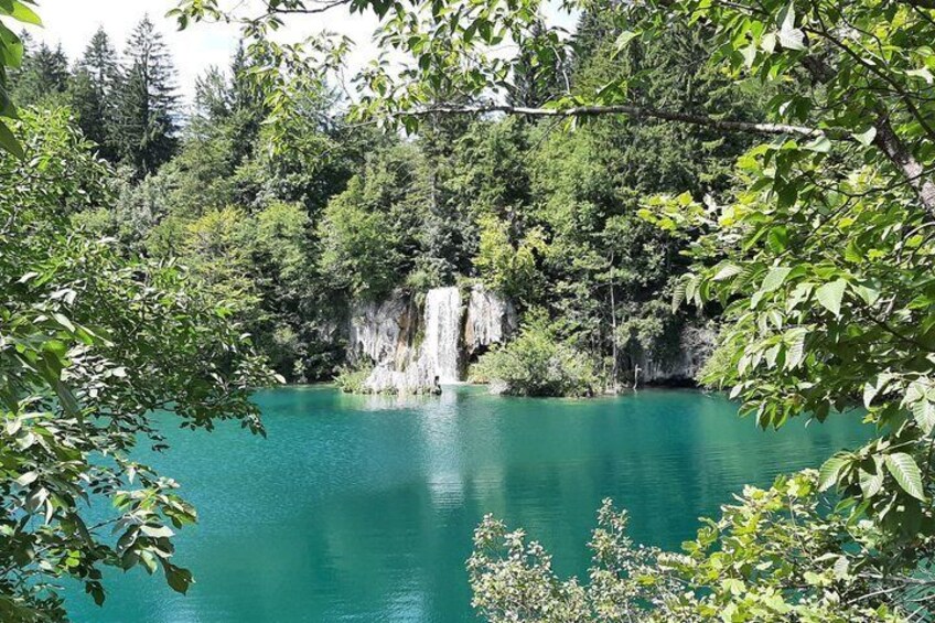 A turquoise lake with a waterfall surrounded by dense forest. 3