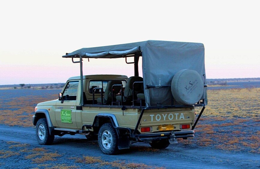 A Toyota off-road vehicle with a roof tent and spare tire on the back, parked on a dirt road. 1