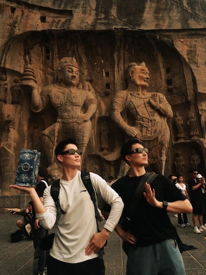 Two people standing in front of a large rock carving with two figures. 1