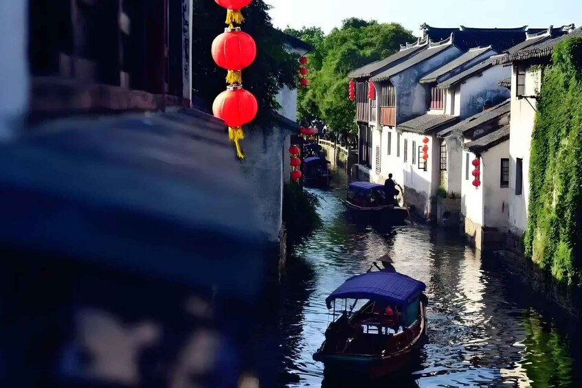 A narrow waterway flanked by traditional buildings with red lanterns, a boat with a blue canopy, and a bridge in the distance. 3