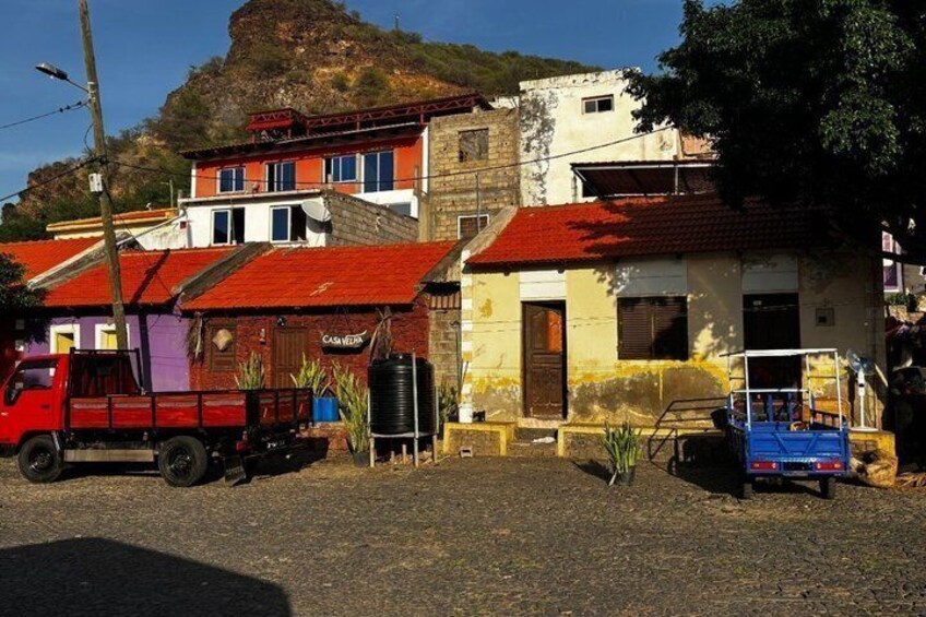 A rural street with colorful buildings, a red truck, and a blue cart. 2