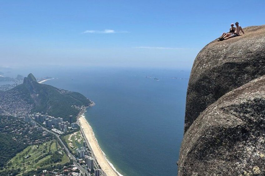 A coastal city with a prominent rock formation, a beach, and a distant mountain peak. 2