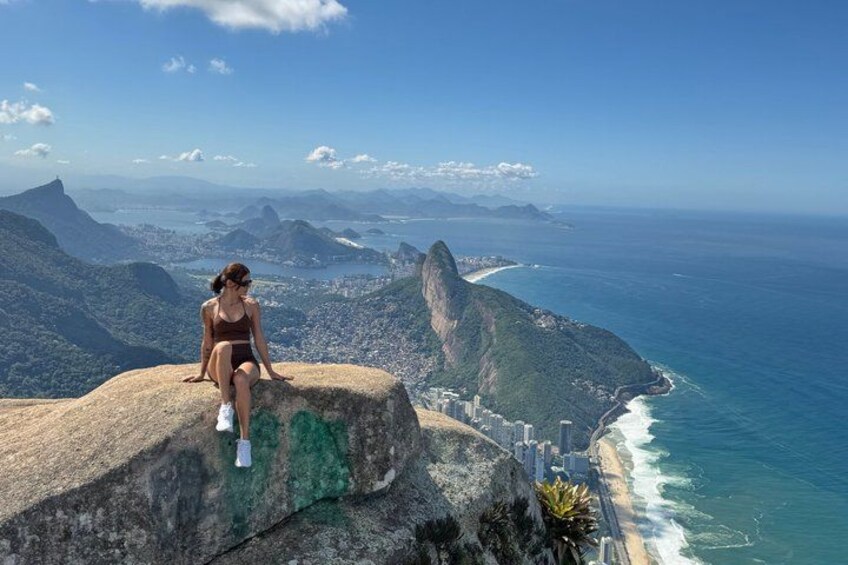 A person sitting on a rock overlooking a coastal city with a prominent mountain and ocean. 3